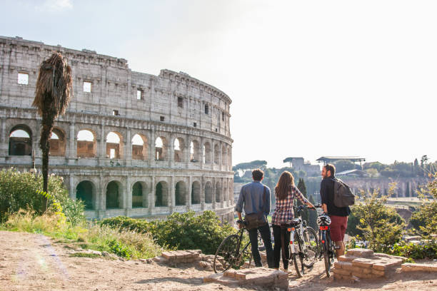 three happy young friends tourists with bikes at colosseum in rome having fun